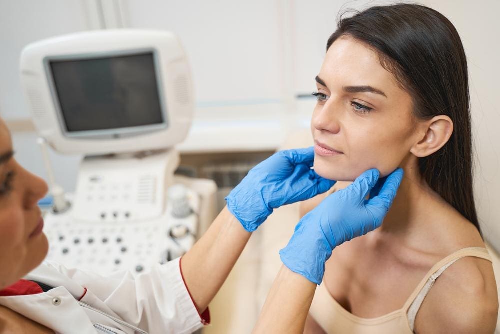 A patient receives a thyroid examination while seated beside an ultrasound machine.