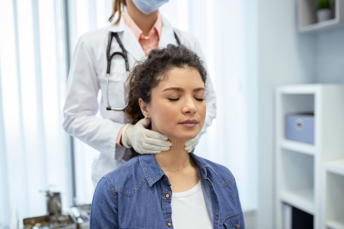 An endocrinologist examines the throat of a young woman in a medical office.