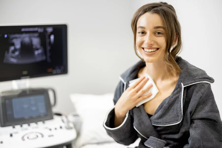 A woman smiles after a thyroid ultrasound showing significant nodule volume reduction after RFA.