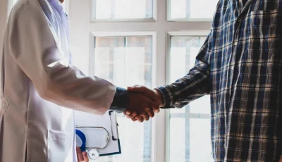 A patient shakes a doctor’s hand in a hospital or clinic hallway.