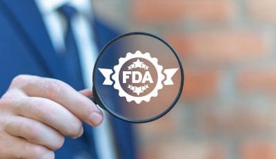 A man holds a magnifying glass with the FDA logo in the center.