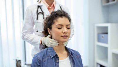 An endocrinologist examines the throat of a young woman in a medical office.